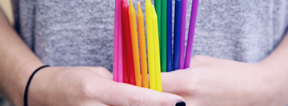 Photo of someone with black nail polish holding thin candles in rainbow colours