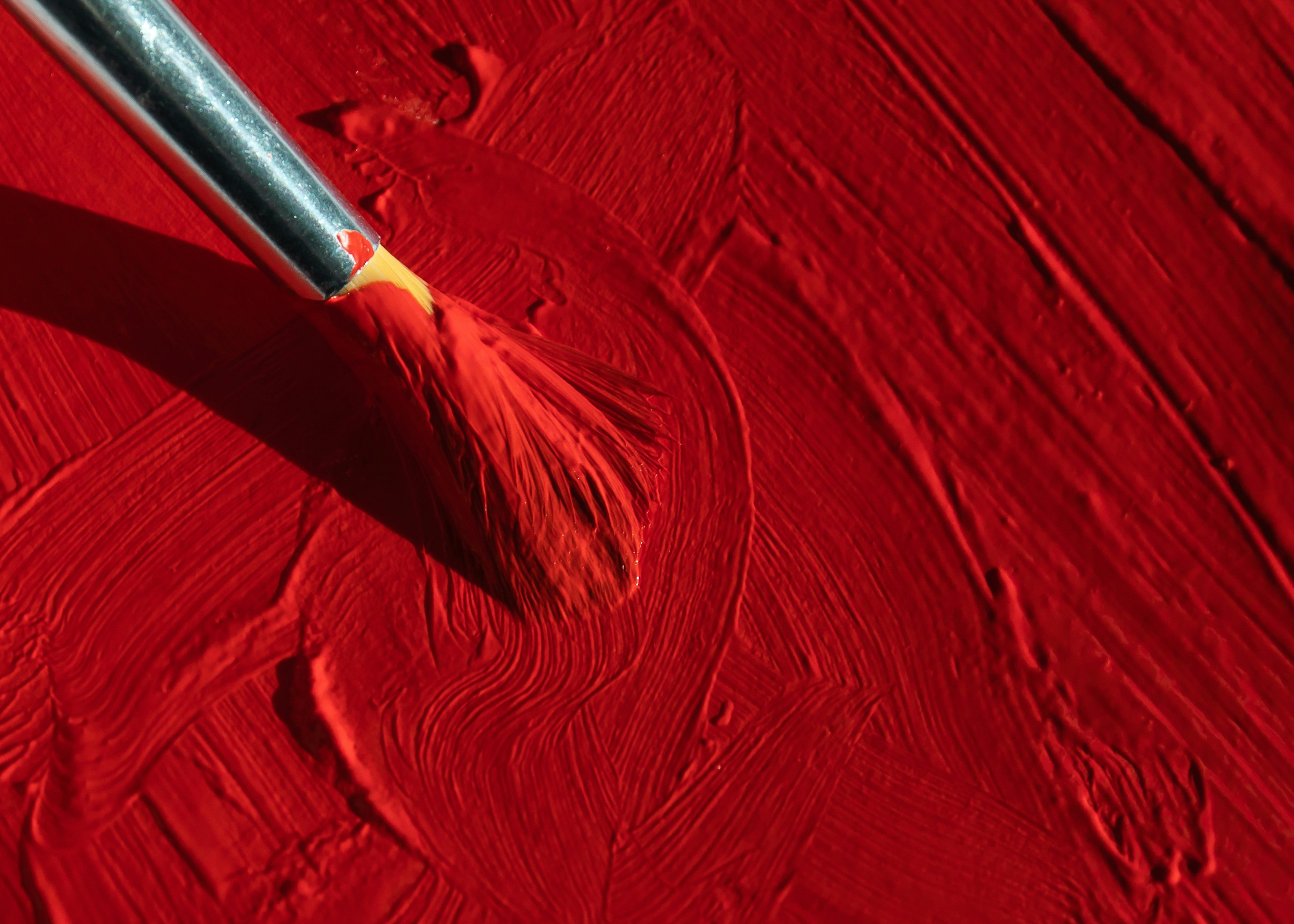 Photo of a paint brush painting on a surface with thick red paint. 