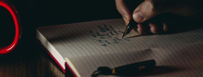 Darkly lit photo of a hand writing in a journal with a fountain pen.